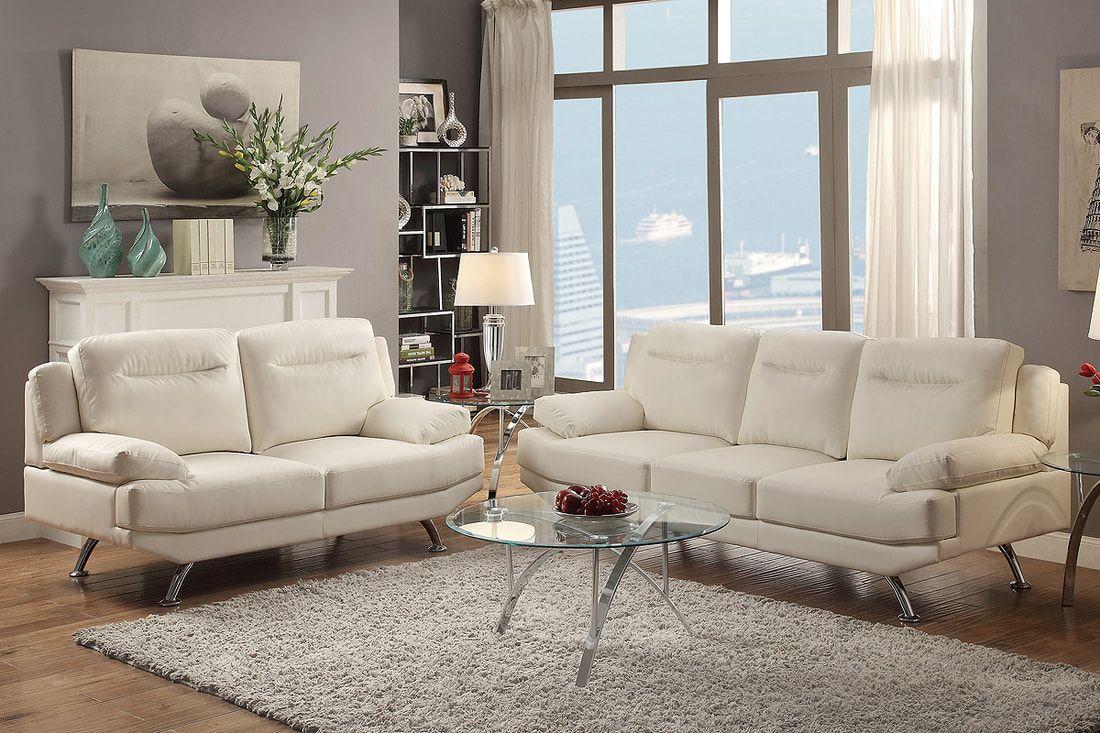 Modern living room with white sofas, glass coffee table, and large windows overlooking the city.
