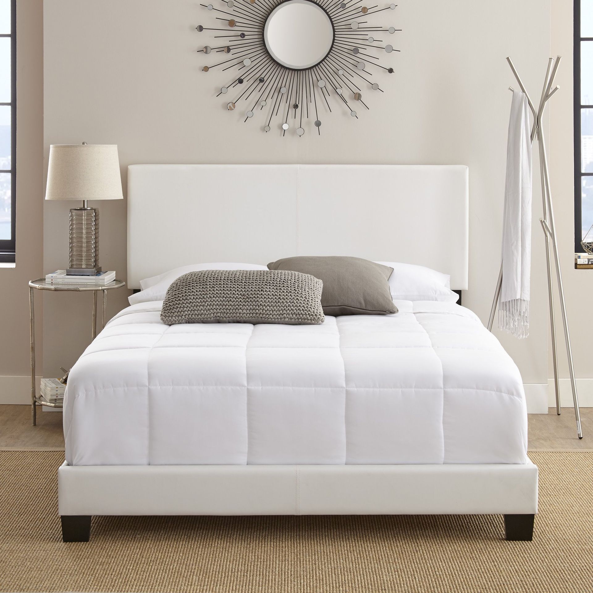 Modern bedroom with white bedding, decorative pillows, and sunburst mirror above headboard.